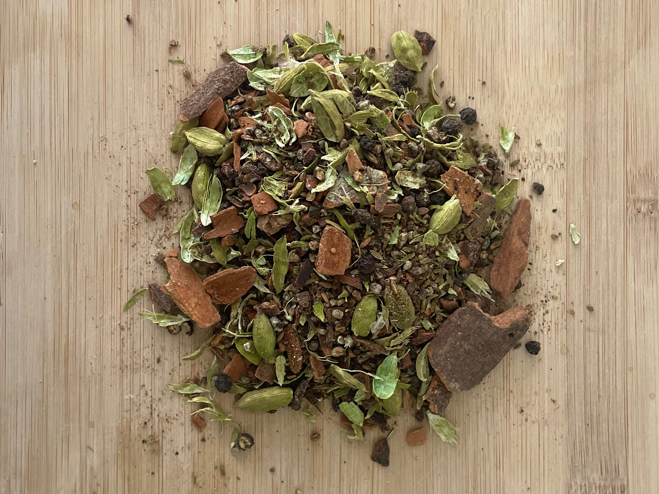 A mixture of spices (masalas) sitting on a wooden board, including cinnamon, cardamom, cloves, fennel, star anise, black pepper, and nutmeg