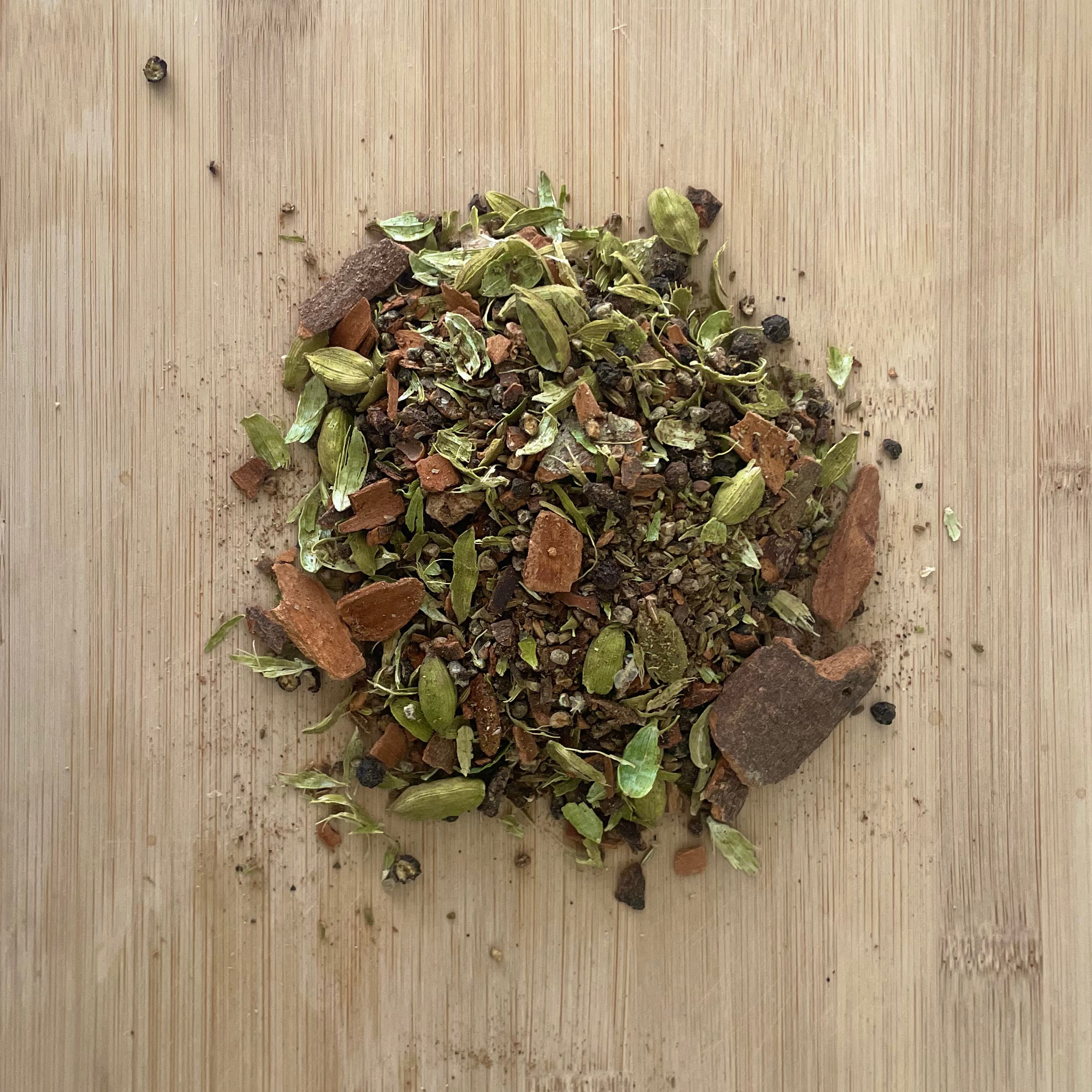 A mixture of spices (masalas) sitting on a wooden board, including cinnamon, cardamom, cloves, fennel, star anise, black pepper, and nutmeg